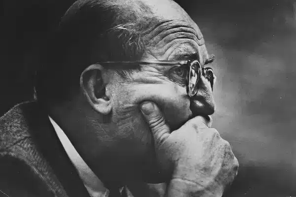Black and white side profile of an older man with glasses resting his chin on his hand, appearing deep in thought.