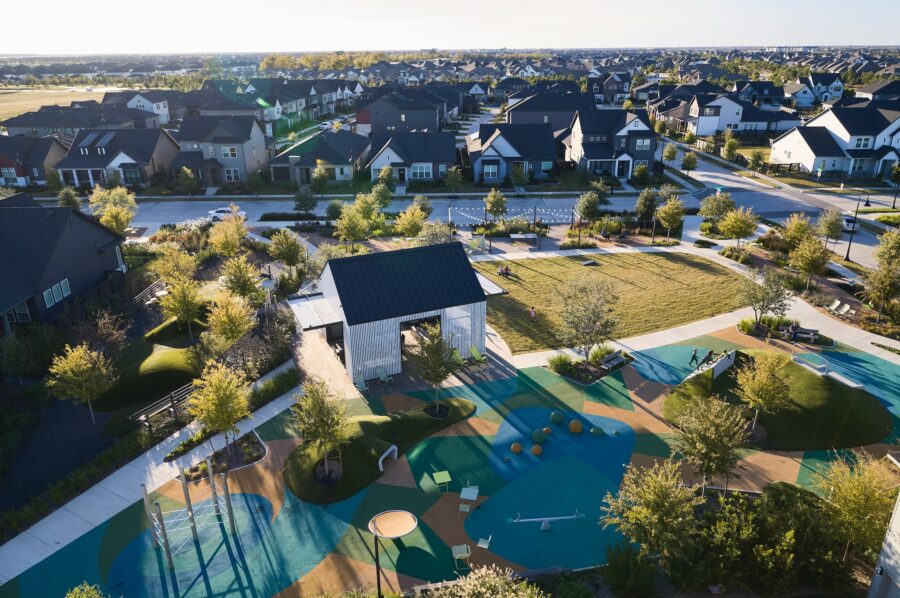 Aerial view of a neighborhood park, featuring a playground, seating area, green spaces, and surrounded by suburban houses.
