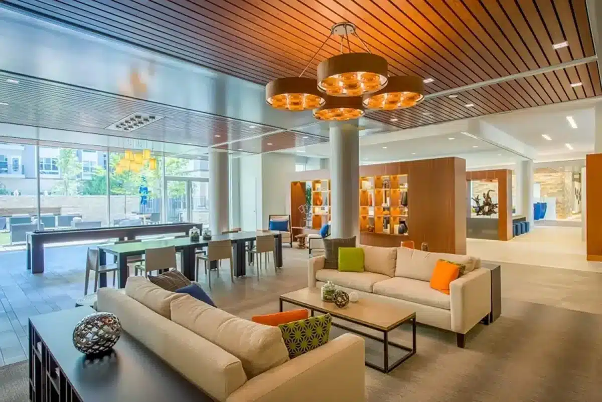 Modern lounge area with beige sofas, colorful cushions, coffee tables, a pool table, and large windows providing natural light.