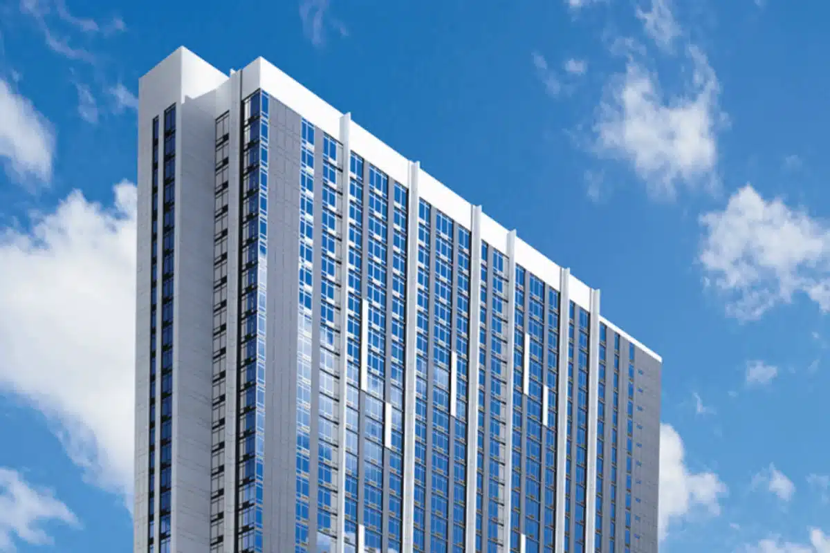 A tall modern Honolulu Condo Tower with many windows stands against a blue sky with scattered clouds, reflecting the innovative design of Howard Hughes.
