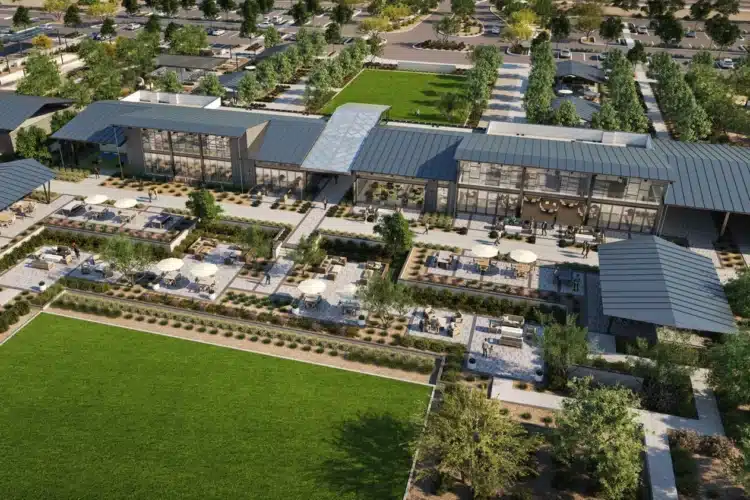 Aerial view of a modern building complex in Teravalis, a master-planned community near Buckeye, featuring outdoor seating areas, landscaped gardens, and a large grassy lawn, all surrounded by trees and parking lots.
