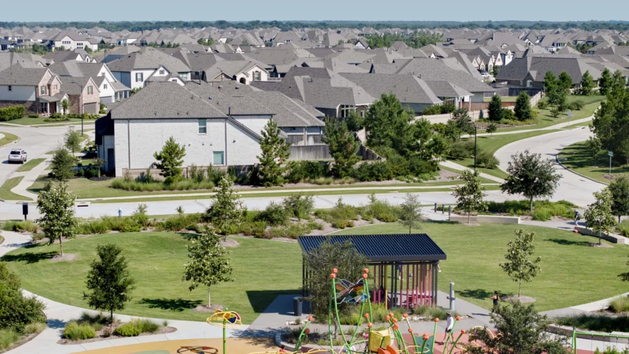 Aerial view of a suburban neighborhood with rows of houses, green spaces, trees, and a playground with colorful equipment in the foreground.