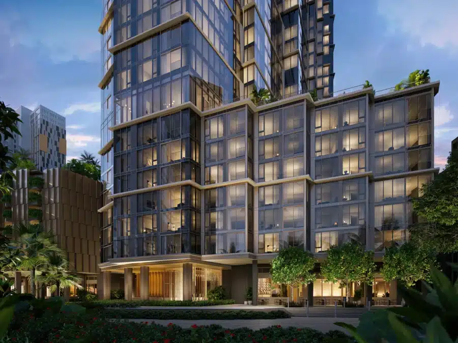 Modern glass-fronted high-rise building with multiple lit windows and greenery at its base, captured at dusk.