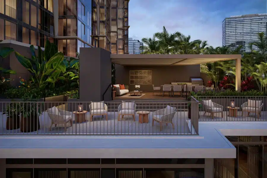 Outdoor terrace with lounge seating, dining area, grill, and lush greenery, surrounded by modern buildings at dusk.