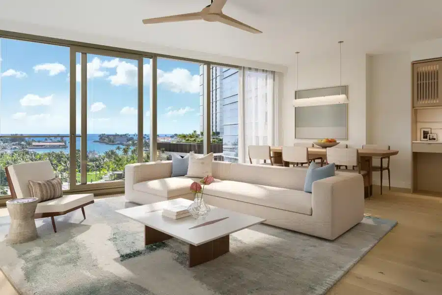 Modern living room with a beige sofa, white coffee table, floor-to-ceiling windows overlooking the ocean, and an adjacent dining area with a table and chairs.