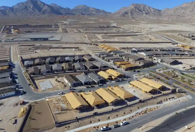 Aerial view of a residential housing development under construction in a desert area, with partially built homes and surrounding mountains.