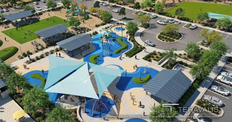 Aerial view of a community park with shaded play areas, splash pad, green spaces, seating areas, and parking lot; people are enjoying various outdoor activities.